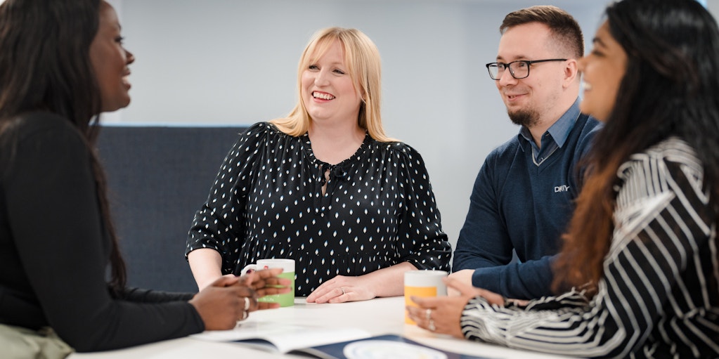 Four professionals sitting around a meeting table and smiling