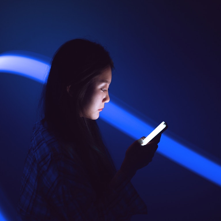 Young Asian woman using smartphone on the holographic background.