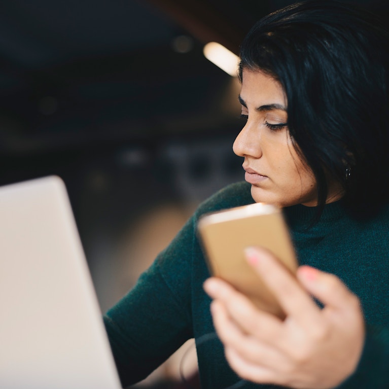 Businesswoman holding smart phone while writing in book in office