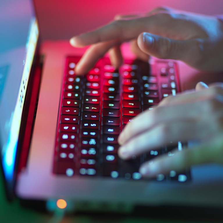 Hacker typing on illuminated laptop keyboard at office