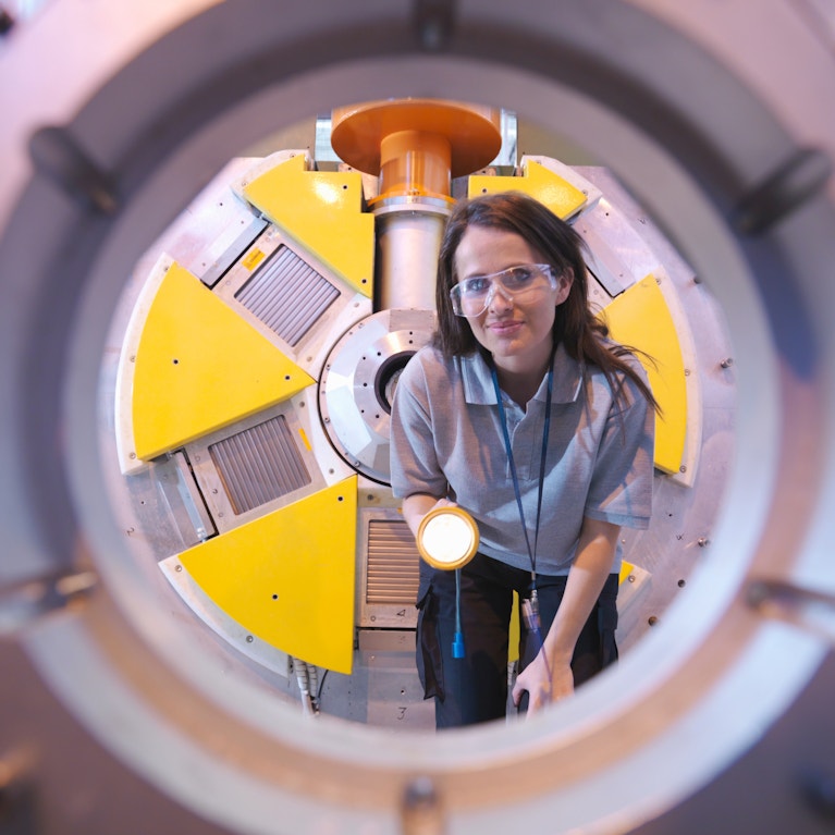 Woman smiling holding flashlight looking through machinery