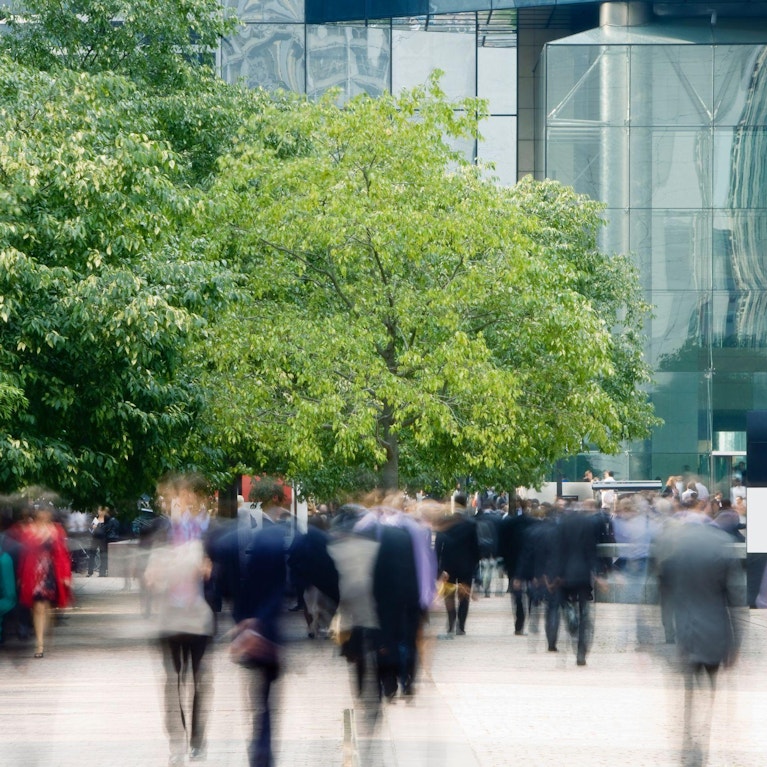 Blurred view of people walking towards office building in plaza with trees
