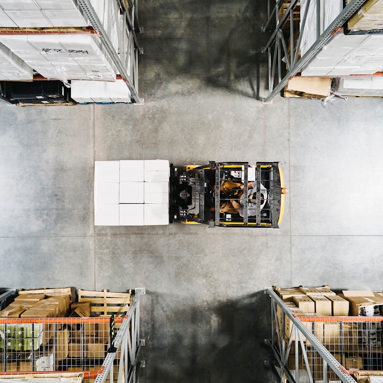 Overhead view of warehouse worker moving pallet of goods with forklift in warehouse